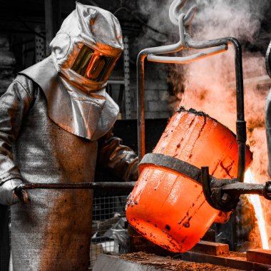 In a foundry workshop. A worker protected by a safety suit pours the molten metal into a mold clipart