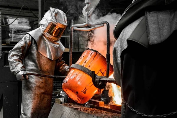 ファウンドリ ワークショップで安全スーツで保護された労働者が溶融金属を型に流し込む — ストック写真