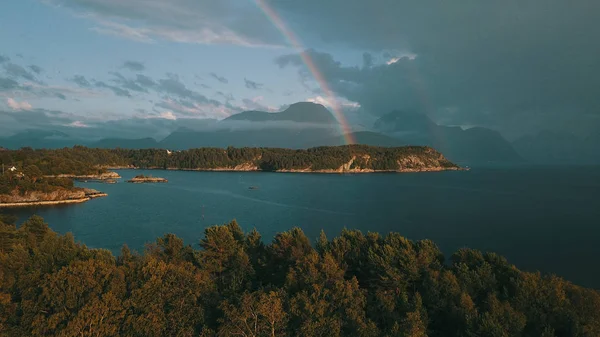 Dağların arka planında gökkuşağı, önplanda küçük bir kasabanın kaya koyunda. Efendi Romsdal, Norveç 2019