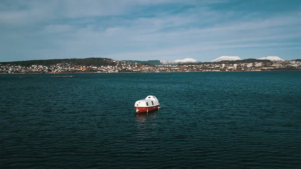 Bir cankurtaran botu, körfezin yanında demirlemiş. Arka planda Norveç 'teki karlı dağların arka planına karşı bir şehir.