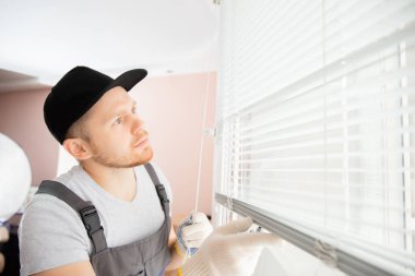 İnşaat işçisi evdeki beyaz camlara jaluzi takıyor.