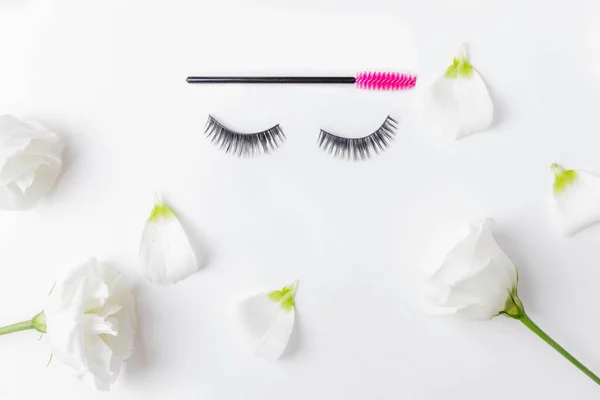 假睫毛延伸与粉红刷在白花的背景，顶视图。 美的概念 — 图库照片