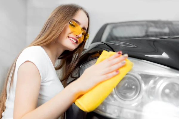 Car wash service, worker beautiful girl polishes and clean microfiber headlights on black auto — Stock Photo, Image