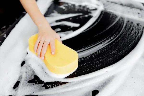 Bakgrund hand hålla svamp över svart bil för tvättning vitt skum — Stockfoto