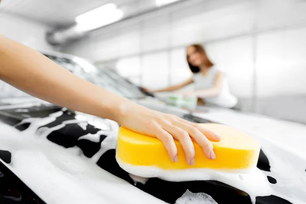 Worker beautiful woman cleaning auto black foam with yellow sponge. Car washing service