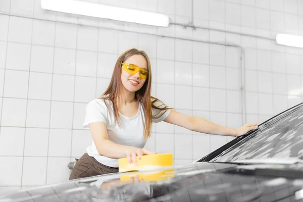 Pracovnice krásná žena čištění auto černá pěna se žlutou houbou. Služba mytí aut — Stock fotografie