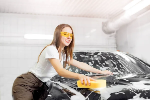 Autowäsche. Arbeiter schöne Frau Reinigung Auto schwarzen Schaum mit gelben Schwamm — Stockfoto