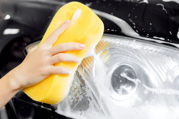 Ručně žena auto mytí pěna se žlutými houbovými světlomety — Stock fotografie