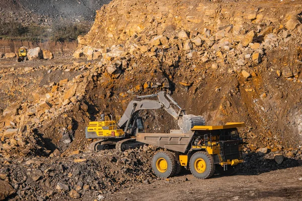 Hydraulic excavator loads gold into body of large yellow mining truck. Open pit mine industry — Stock Photo, Image