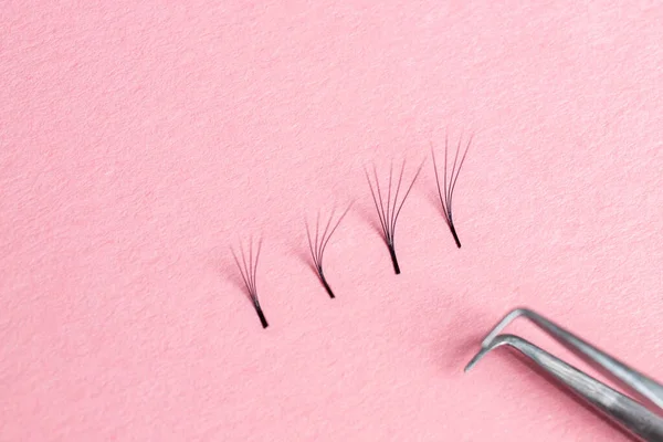 Bunches of fake lashes and tweezers on pink background. Eyelash extension procedure — Stock Photo, Image