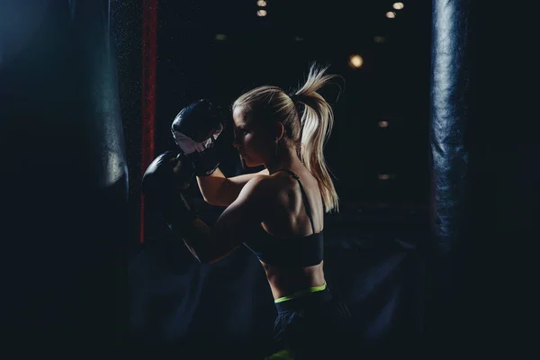 Fuerte atlética joven rubia está entrenando golpes de autodefensa en guantes de boxeo. Concepto deporte femenino — Foto de Stock