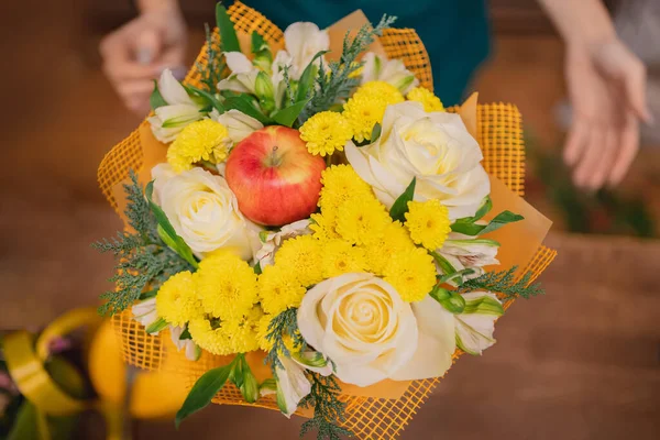 Florist makes autumn bouquet of roses flowers, apples red, green and yellow leaves