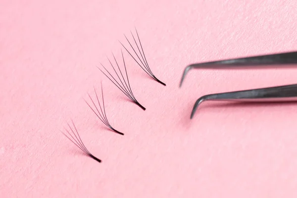 Bunches of fake lashes and tweezers on pink background. Eyelash extension procedure — Stock Photo, Image