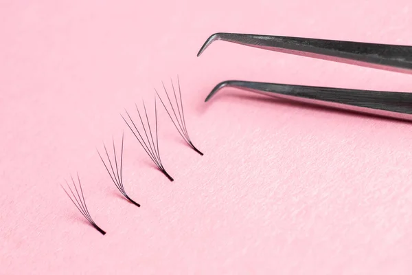 Bunches of fake lashes and tweezers on pink background. Eyelash extension procedure
