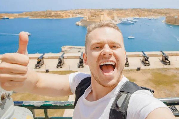 Valletta Malta happy tourist man in glasses makes selfie photo on background panorama gun bay