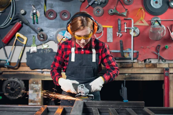 Hermosa mujer joven ingeniero artesano se encuentra en delantal en el fondo de las herramientas para la elaboración. Concepto de pequeña empresa en garaje sala industrial — Foto de Stock