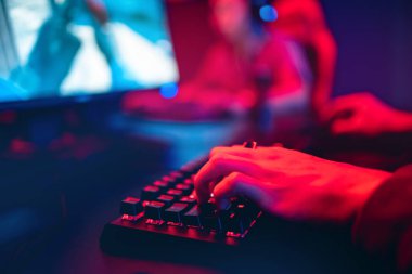 Profesyonel çevrimiçi oyuncu parmaklarını mekanik klavye ile neon rengi bulanık arka planda tutuyor. Yumuşak odak, arka görünüm