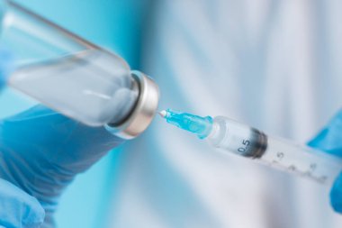 Doktorun elinde mavi eldivenli beyaz önlüklü şırınga ve aşı var. Enjeksiyon konsepti
