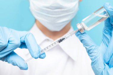 Güzellik doktoru mavi arka planda şırınga tutuyor. Dudak büyütme enjeksiyonu, yaşlanma önleyici serum, estetik ameliyat.