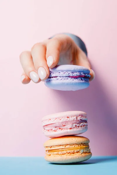 Bonitas mãos menina com unhas manicure moda segurando cor macaroon bolo através de buraco no fundo rosa — Fotografia de Stock