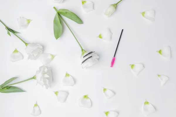 Falsche Wimpernverlängerungen mit rosa Pinsel auf weißem Blumenhintergrund, Draufsicht. Schönheitskonzept — Stockfoto