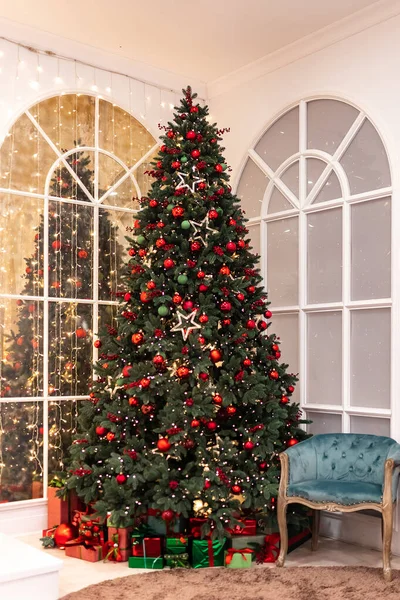 Lange kerstboom versierd met rode ballen, sterren, verlichting, geschenken liggen hieronder — Stockfoto