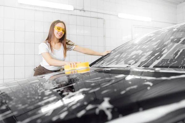 Worker beautiful woman cleaning windshield foam with sponge. Car washing service — Stock Photo, Image