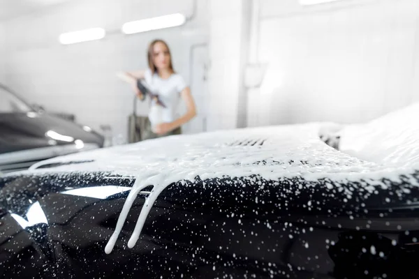 Car washing service. Worker woman cleaning auto using foam high pressure water
