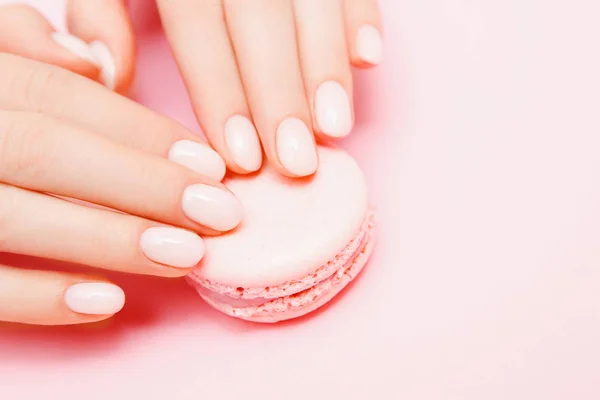 Elegante manicure feminina na moda em fundo rosa. Menina segura as mãos biscoitos de macaron. Vista superior, flat lay — Fotografia de Stock
