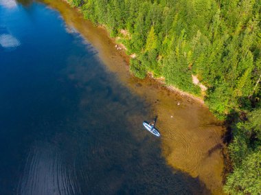 Kürek çeken bir kadın mavi deniz suyunda kürek çekiyor. Gökyüzü üst görünümü kürekleri
