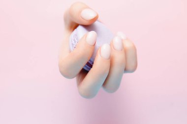 Kız menekşe makarna kurabiyelerinin elini tutuyor. Pembe arka planda şık moda kadın manikürü