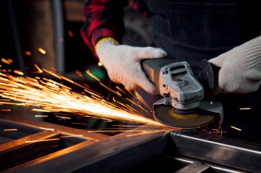 Fabrikadaki çelik yapıya elektrik tekerleği sürten işçi el, hafif kıvılcım.