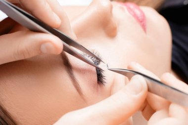 Kirpik uzatma prosedürü. Cımbız ustası güzel bir kadına sahte kirpik takar.