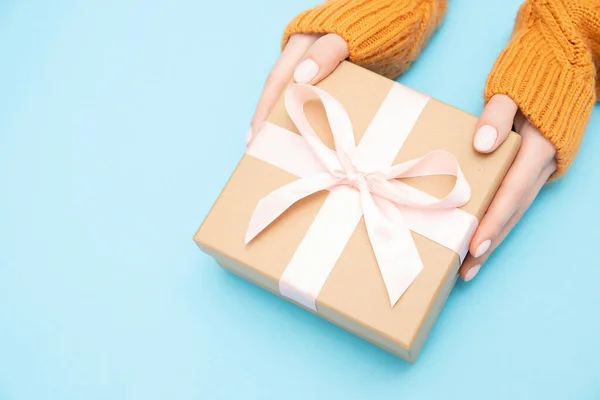 Hermosas manos niña sostienen caja de regalo presente papel artesanal con lazo rosa sobre fondo azul, vista superior. Concepto Navidad, Año Nuevo — Foto de Stock