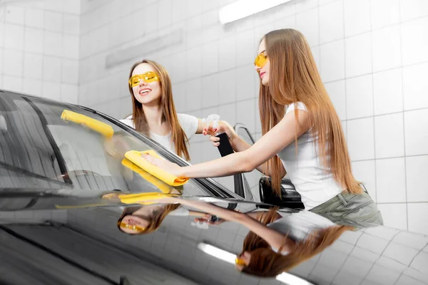 Hermosas mujeres sonriendo lavando la ventana del coche spray limpio — Foto de Stock