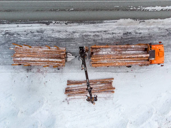 Loader truck for transporting wooden logs in winter, packs trees. Aerial top view.