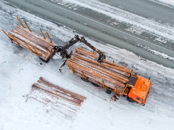 Loader truck for transporting wooden logs in winter, packs trees. Aerial top view.