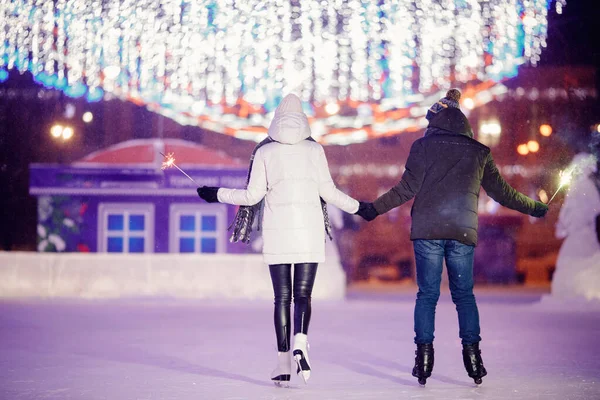 Pattini invernali, coppia amorevole che si tiene per mano e rotola sulla pista di pattinaggio. Illuminazione in sottofondo, notte. Allenamento concettuale. Vista posteriore — Foto Stock