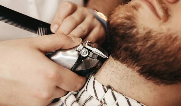Barber shaves his beard to hipster man in barbershop. Toned photo, vintage style — Stock Photo, Image