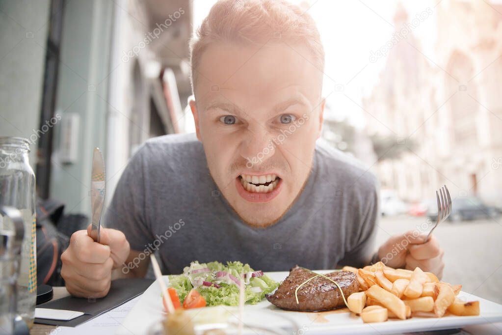 Very hungry man prepares to eat juicy steak and French fries, holds knife and fork