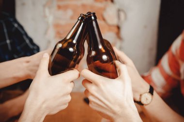 Friends drink craft beer in pub, clinking bottles of chin-chin clipart