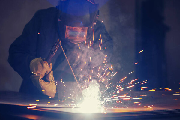 Professional welder performs welding work on metal in protective mask. Industrial worker concept