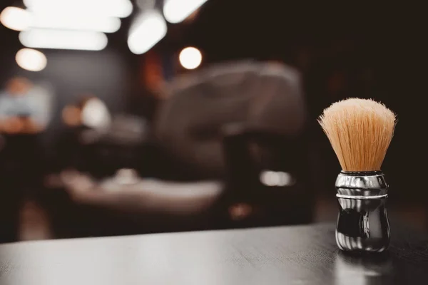 Brush for shaving beard along with bowl, blurred background of hair salon for men, barber shop. — Stock Photo, Image