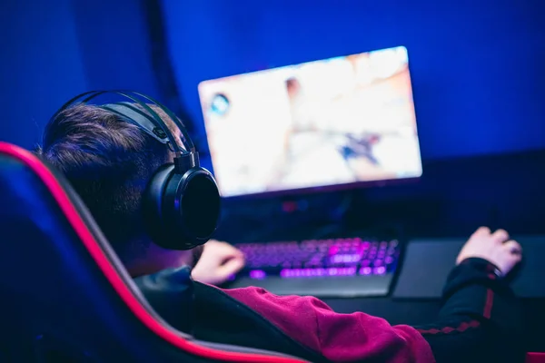 Jugador profesional jugando torneos de juegos en línea ordenador PC con auriculares, fondo rojo y azul borrosa —  Fotos de Stock