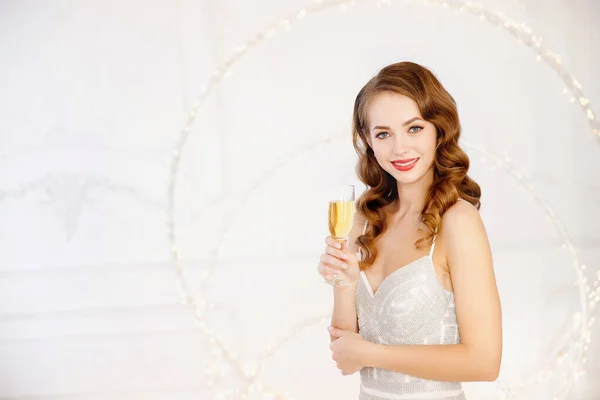 Linda menina morena em vestido de prata no fundo branco desfocado com copo de champanhe comemorando. Conceito sentimento de Ano Novo, Feliz Natal — Fotografia de Stock