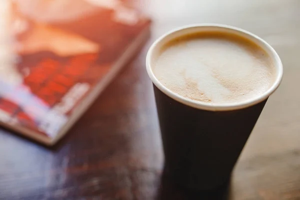 Oberseite Textur aus Schaumstoff und Kaffee-Cappuccino-Latte-Blasen in Pappbecher auf Holztisch, Linsenschlag, Hintergrund ist Magazin — Stockfoto