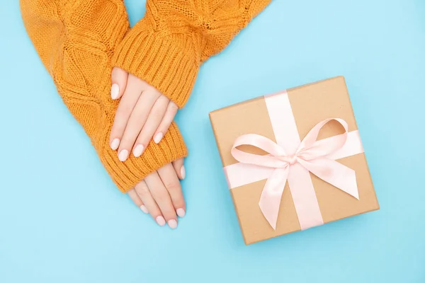 Hermosas manos femeninas con manicura rosa en las uñas en un cálido suéter de punto fondo azul con baht caja artesanal de regalo. Estilo Plano lay — Foto de Stock