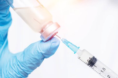 Doktor elinde şırınga ve aşıyı mavi eldivenli, beyaz önlüklü, güneş ışığında tutuyor. Hastalık enjeksiyonu