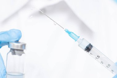 Doktorun elinde mavi eldivenli beyaz önlüklü şırınga ve aşı var. Enjeksiyon konsepti