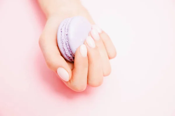 Stijlvolle trendy vrouwelijke manicure op roze achtergrond. Meisje houdt handen violet macaron koekjes — Stockfoto